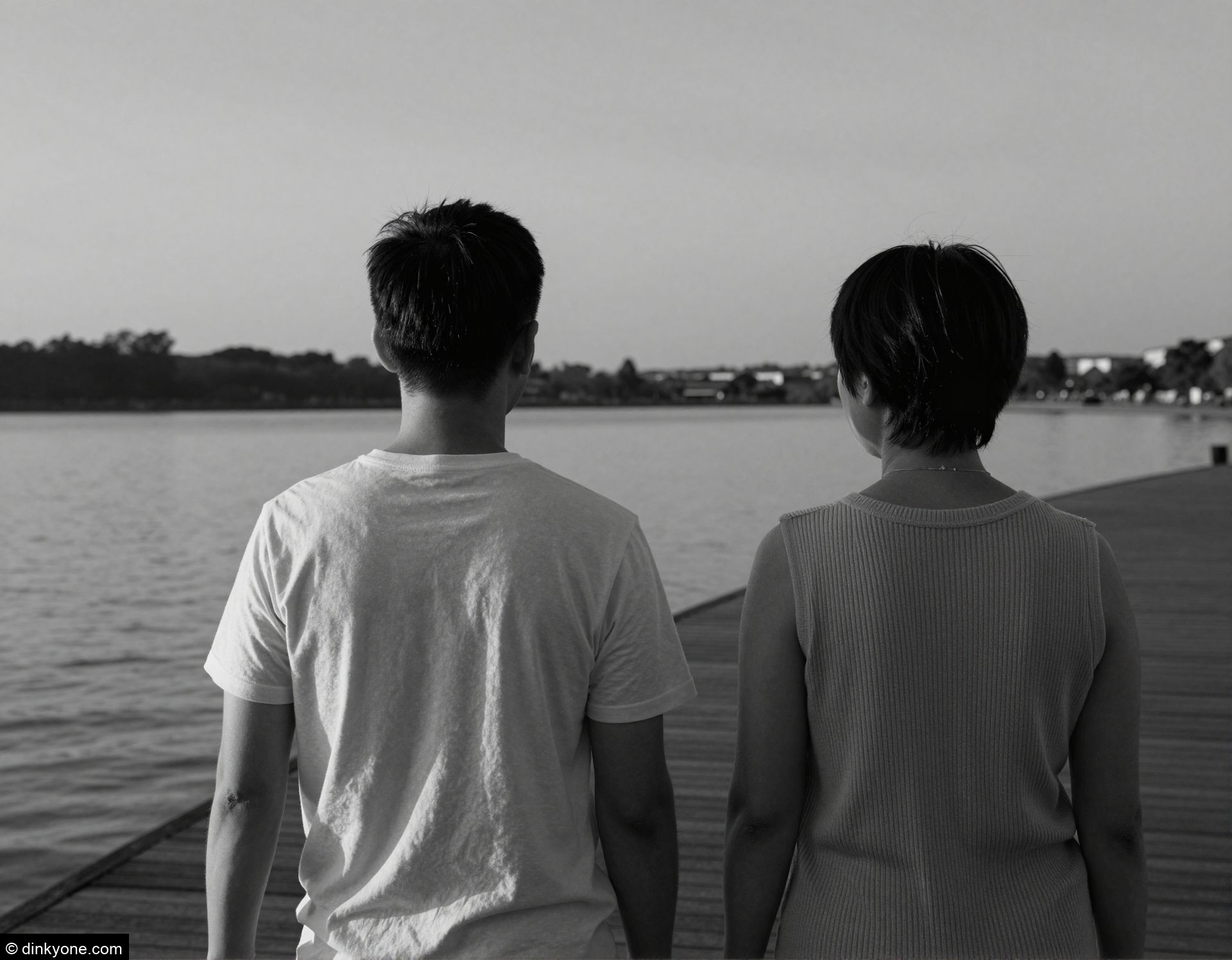 A couple on a lakeside boardwalk during sunset.