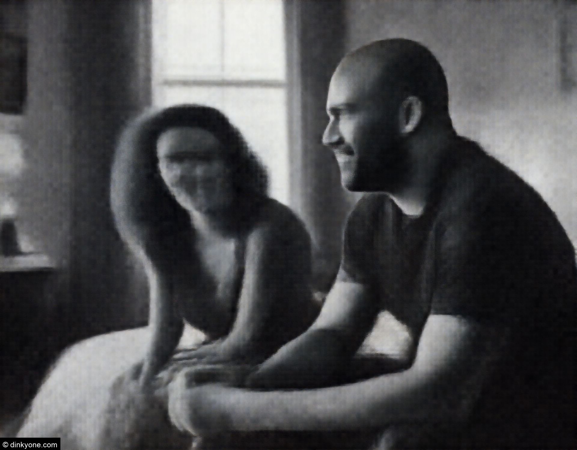 A strong-looking couple in a cosy bedroom with large windows and warm lighting.