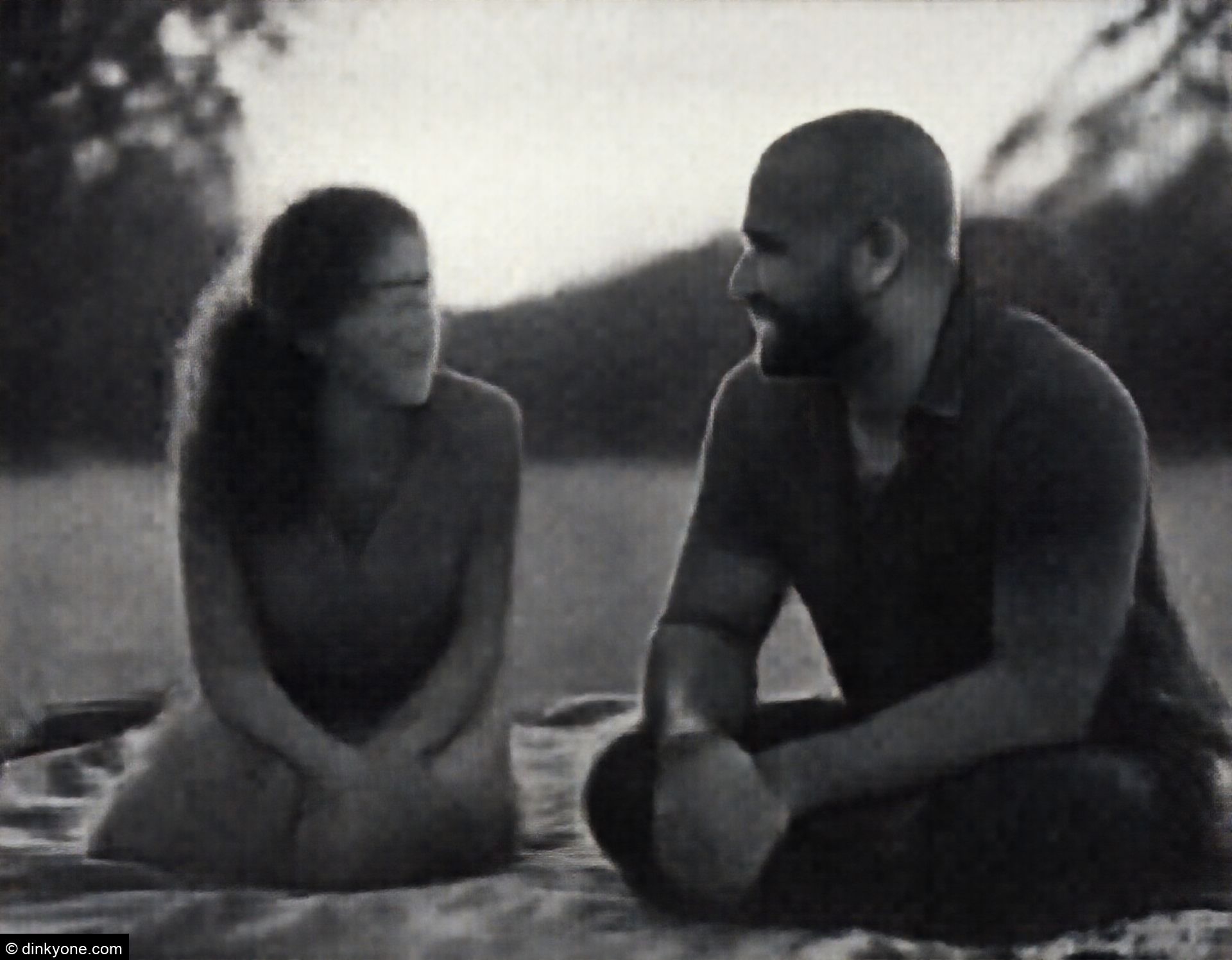 A strong-looking couple on a picnic blanket in a park during sunset.